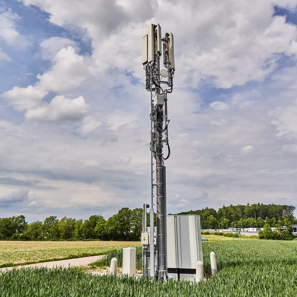 Cell tower with multiple antennas and cables mounted on a tall mast against a cloudy sky.