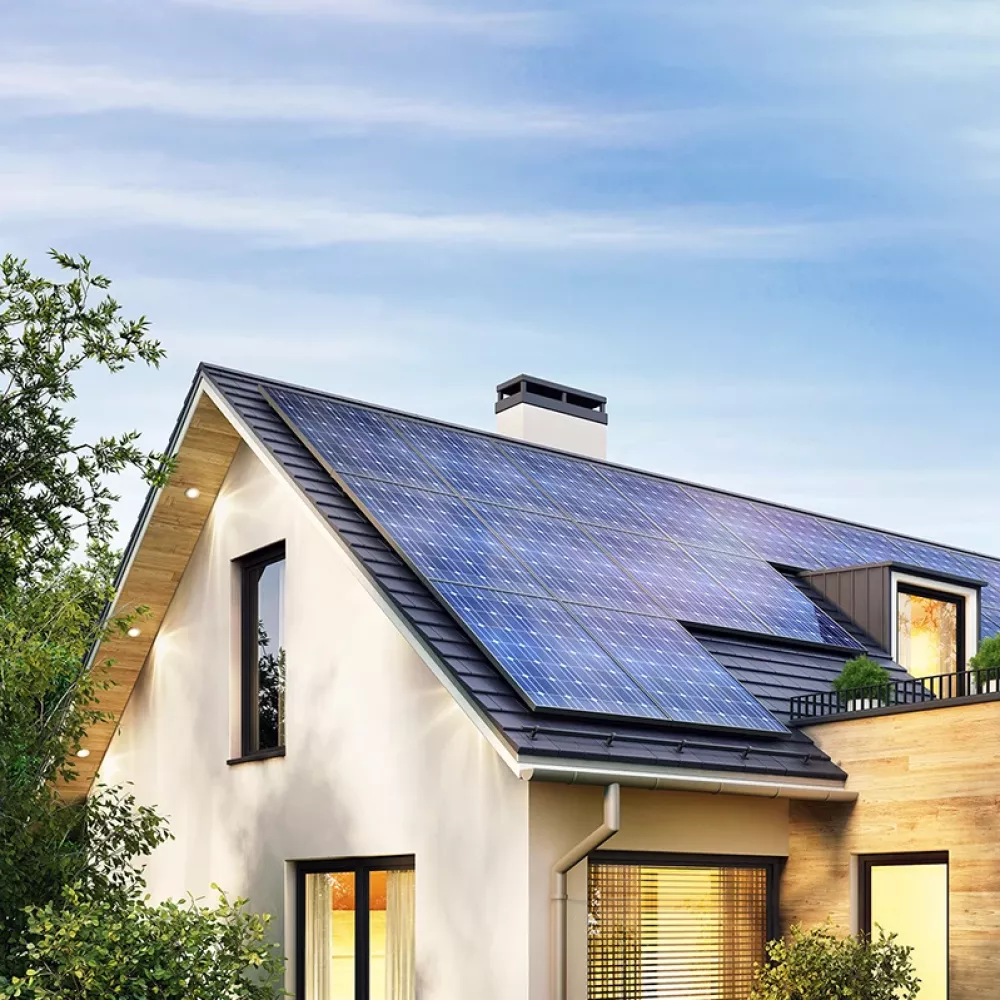Modern single-family house with rooftop solar panels, large windows, and surrounding trees under a clear blue sky.