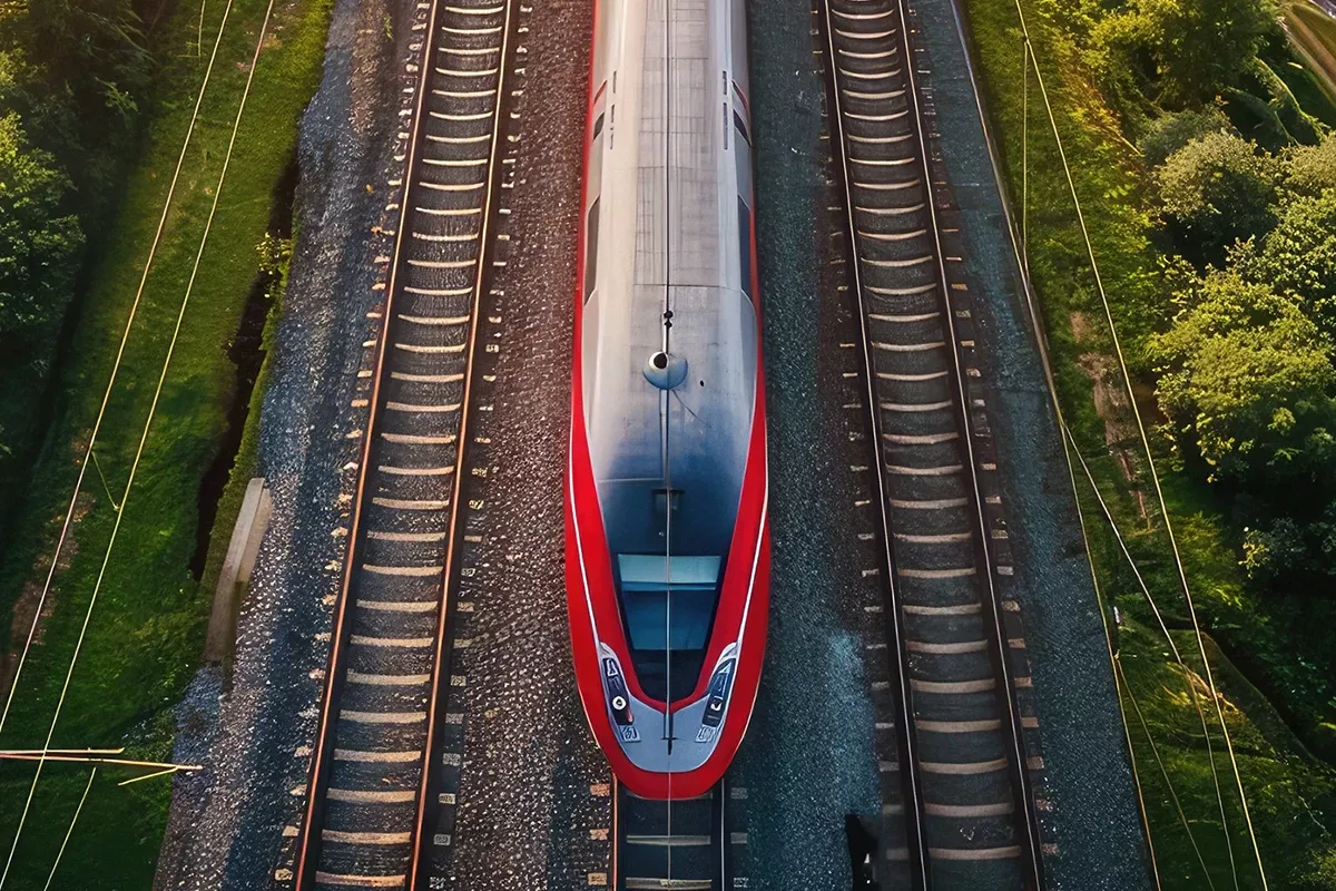 Top-down aerial view of a red high-speed train traveling on railway tracks, surrounded by green vegetation on both sides.